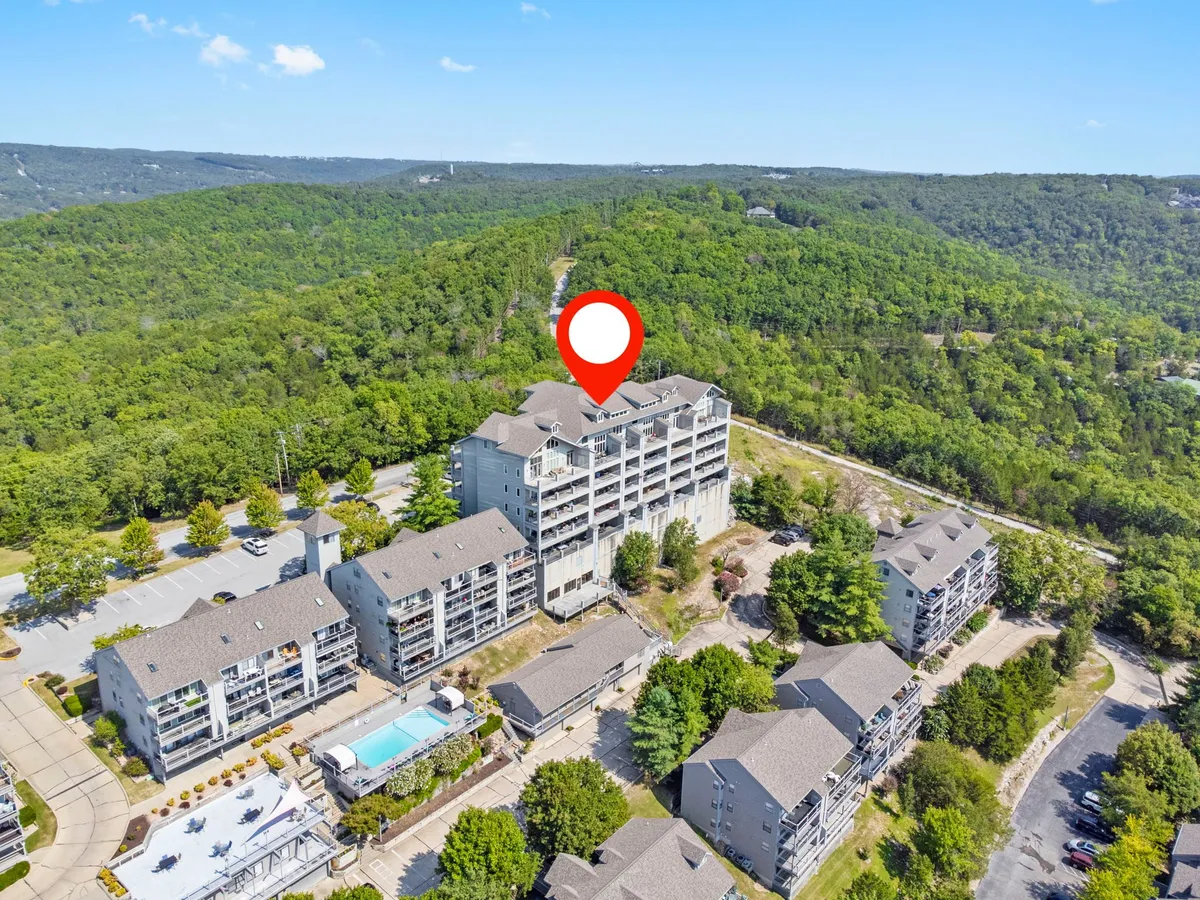 A relaxing exterior scene featuring multi-story resort buildings, a shimmering swimming pool, and lush surrounding greenery. The space invites both exploration and poolside relaxation, reflecting a community-centered resort feel.