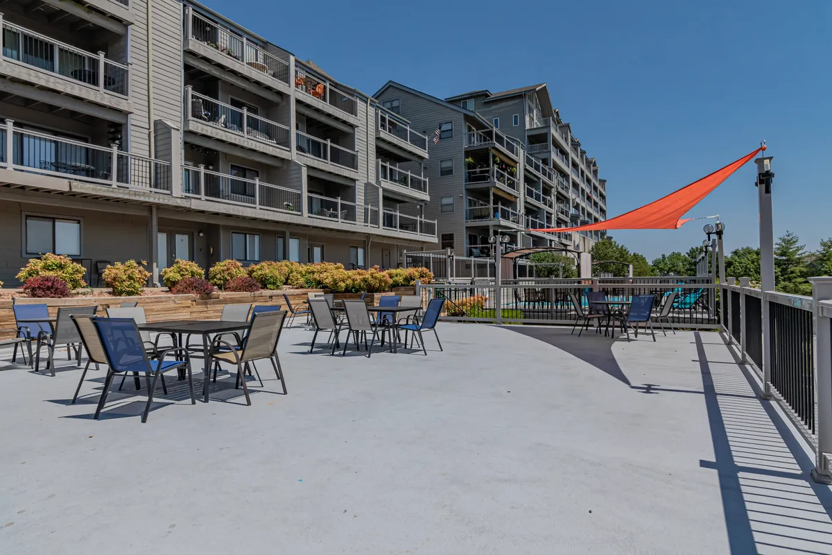 An outdoor seating area with colorful umbrellas, lush potted plants, and modern apartment buildings in the background. The scene is vibrant and casual, featuring spaces ideal for outdoor dining, socializing, or simply relaxing in a tranquil environment.