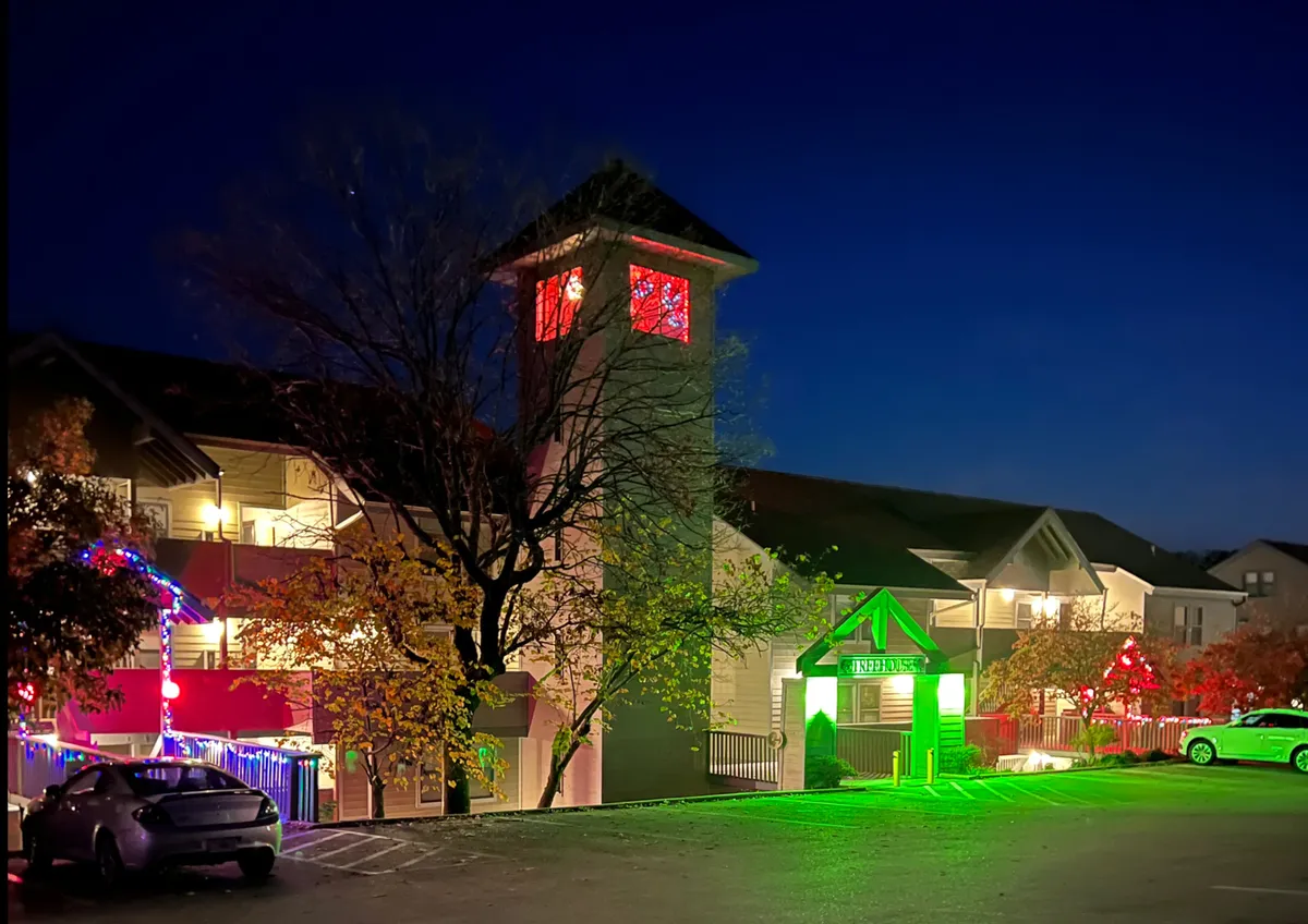 A warmly lit exterior scene featuring decorative lights, a clock tower, and an entrance sign, hinting at lively community spaces and evening activities.