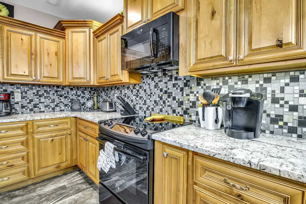 A warm, welcoming kitchen scene with wooden cabinetry, rich granite countertops, a striking mosaic backsplash, and gleaming stainless appliances. The setting feels lively and functional, perfect for both casual baking and hosting elegant dinner parties.