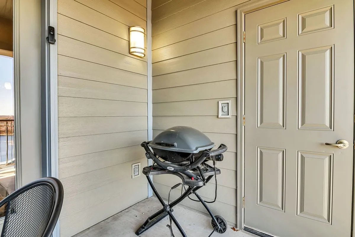 A private exterior patio space featuring a grill, door, and light fixture, ideal for barbecuing, relaxing, and socializing in a laid-back outdoor setting.