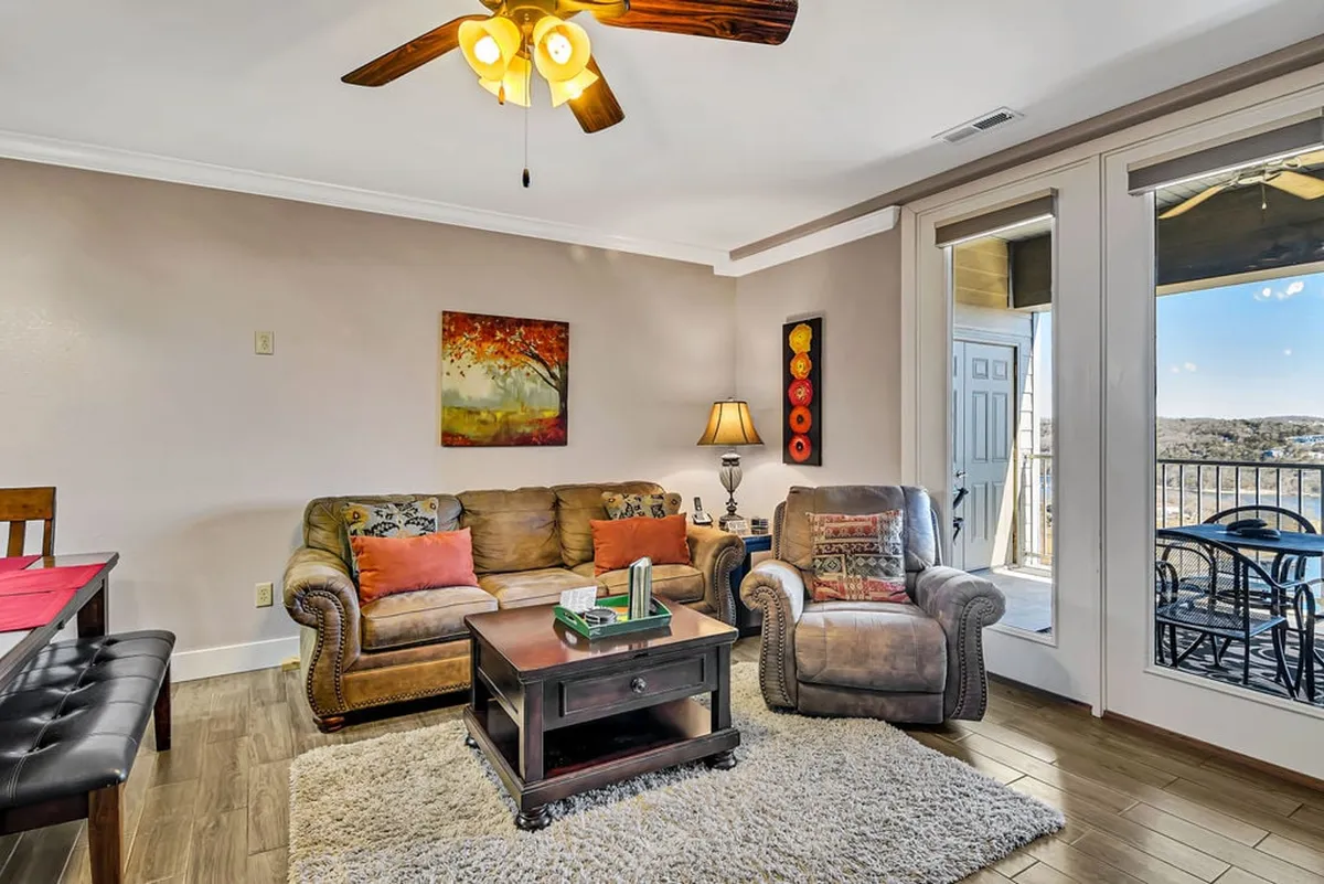 A stylish and welcoming living room with a comfortable sofa, coffee table, lamp, artwork, and a window offering a glimpse of the outdoors. The room feels intimate yet bright, perfect for quiet evenings or lively conversations.