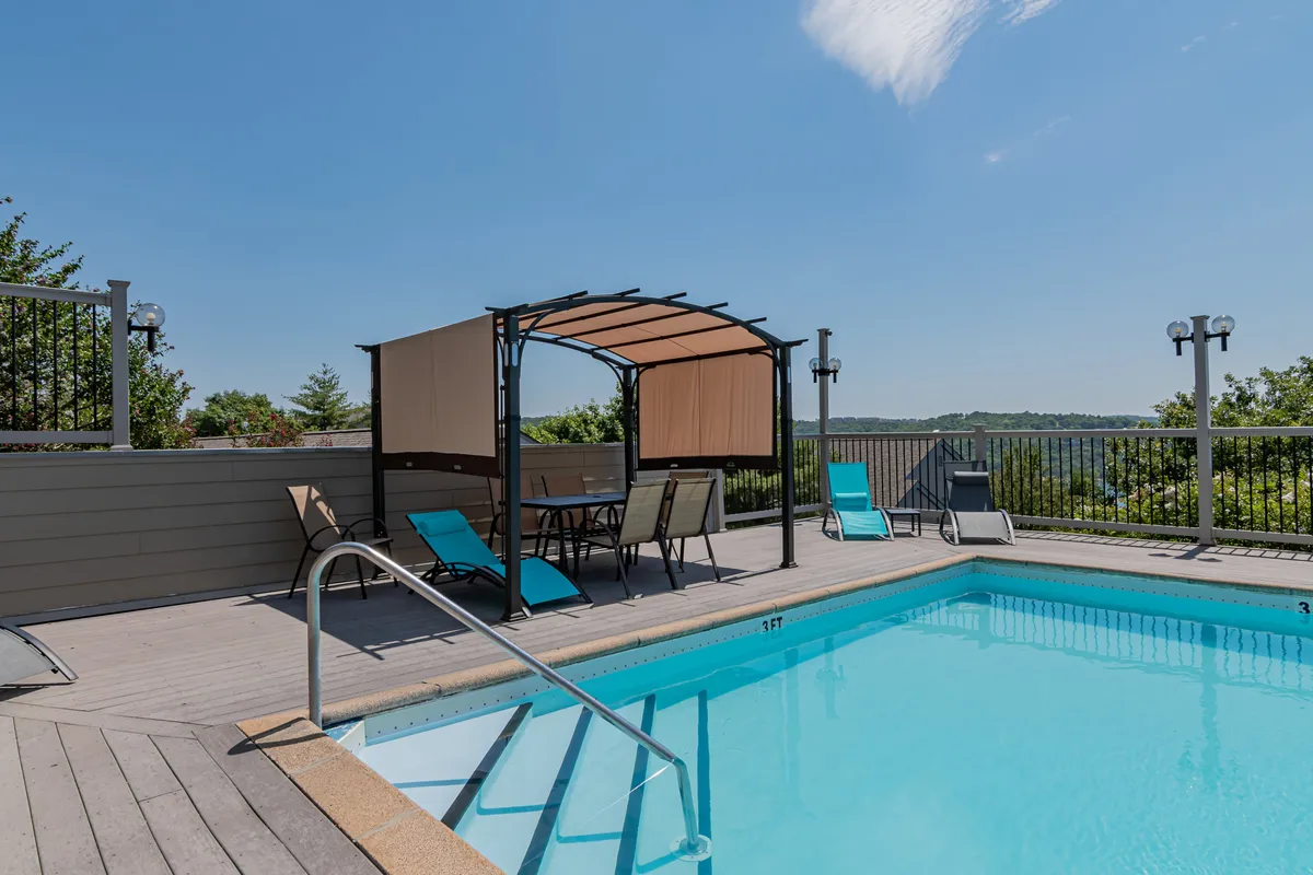 A sparkling swimming pool framed by a canopy structure and ample lounge chairs, with sweeping views of the surrounding landscape. The pool area is inviting and tranquil, ideal for sunbathing, swimming, or relaxing with friends and family.