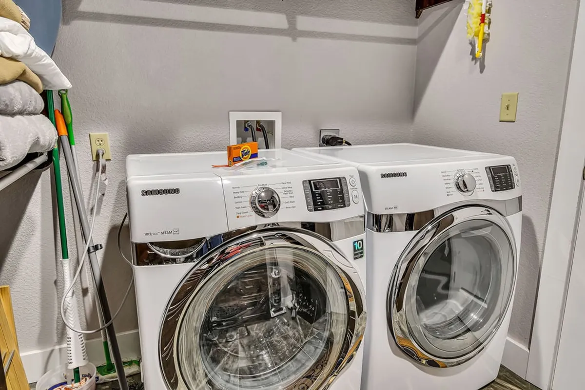 A practical in-suite laundry area fitted with a washer, dryer, detergent box, and shelving unit. The space is neat and efficient, designed for convenience and longer stays.