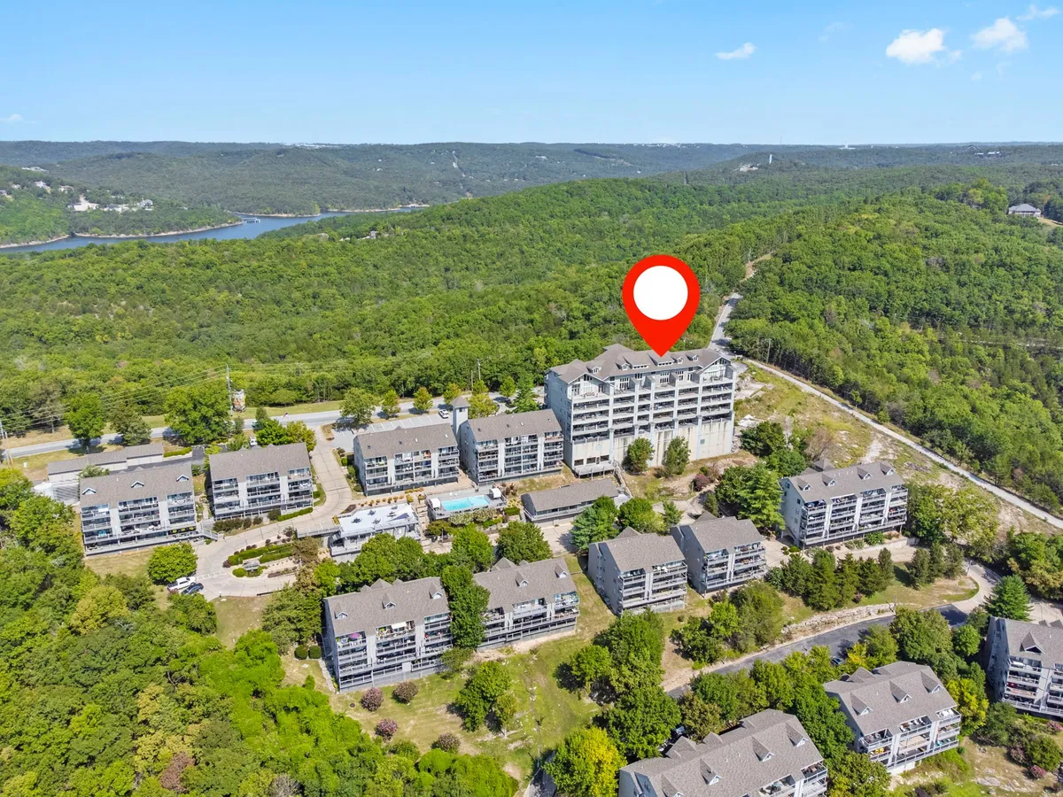Multiple modern condo buildings are nestled among lush greenery, with a clear view of a sparkling swimming pool area. The landscaping and layout imply peaceful walks, community gatherings, and easy access to nature—a welcoming setting for lakeside picnics and outdoor exploration.