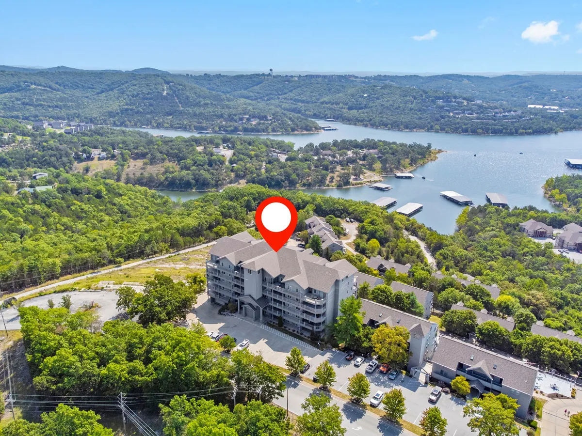 An exterior view featuring the main building nestled among greenery with a clear, expansive view of the lake. The relaxed mood and wide perspective evoke feelings of escape and connection to nature, with suggestions of boating, hiking, and picnicking.