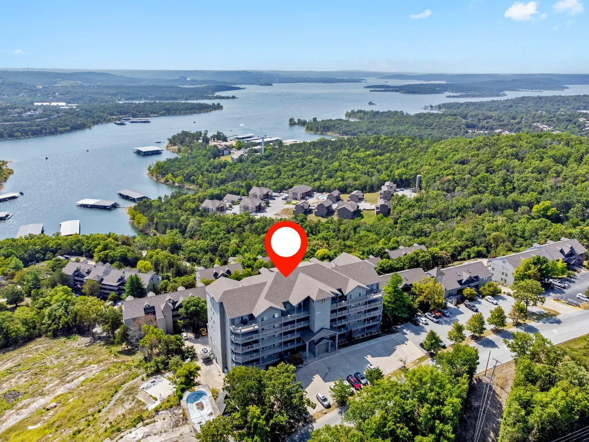 This image shows a serene lakeside scene with a prominent view of the tranquil lake, lush surrounding greenery, and a glimpse of the building structure, possibly the property itself. The atmosphere is peaceful and relaxed, suggesting opportunities for boating, hiking, and outdoor dining by the water.