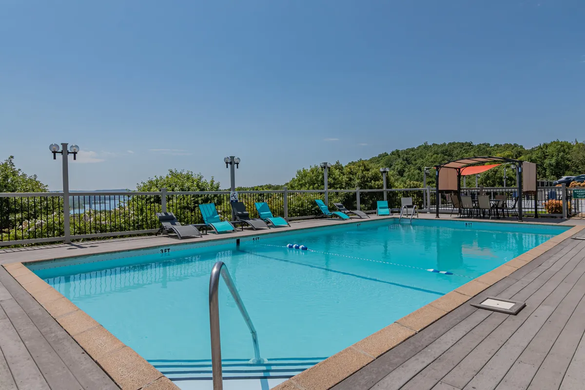 A sparkling outdoor swimming pool surrounded by lounge chairs and a canopy area, nestled amid lush greenery. The pool area appears clean, inviting, and perfect for both relaxation and social gatherings.