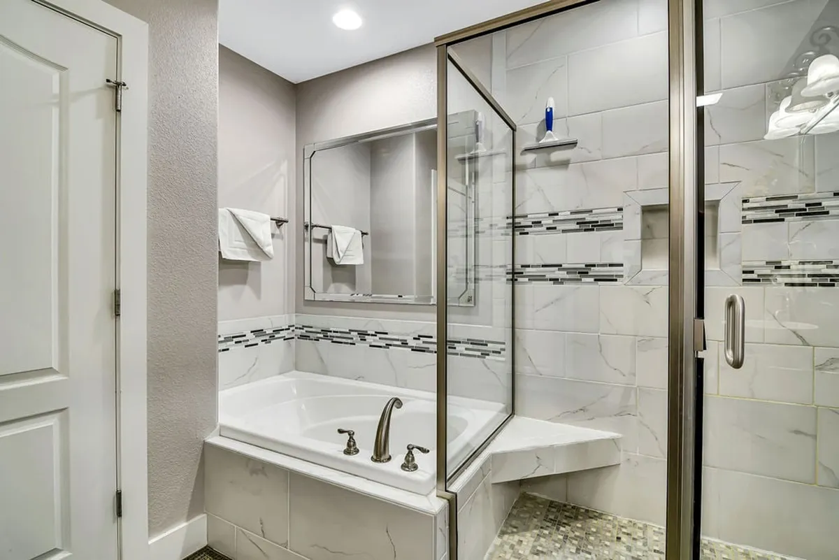 A modern ensuite bathroom showcasing a large soaking bathtub, a glass-enclosed shower, and a mirror above the vanity. Clean lines and soothing tones evoke a spa-like atmosphere, inviting relaxation and self-care.